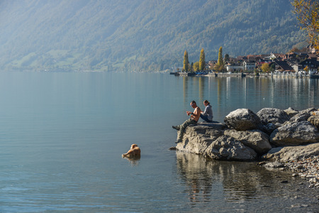 Brienz, Switzerland - Oct 21, 2018. A young couple sitting on rock and playing with the dog on lake side of Brienz, Switzerland.のeditorial素材
