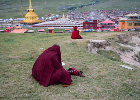 Tibetan monks sitting on the hill and looking at Yarchen Gar in Sichuan, China. Yarchen Gar is the largest concentration of nuns and monks in the world.の写真素材