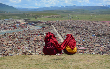 Tibetan monks sitting on the hill and looking at Yarchen Gar in Sichuan, China. Yarchen Gar is the largest concentration of nuns and monks in the world.の写真素材