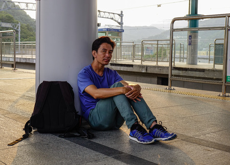 A tired man sitting and waiting the train at railway station in sunset.
