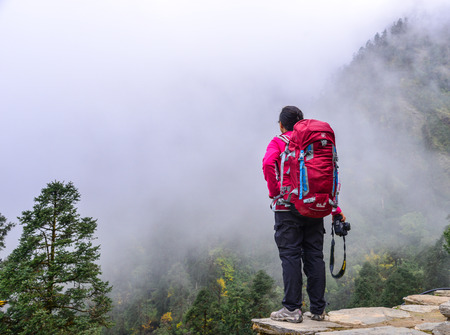 Pokhara, Nepal - Oct 20, 2017. A trekker with backpack looking at the misty forest on mountain in Annapurna Range, Nepal.のeditorial素材