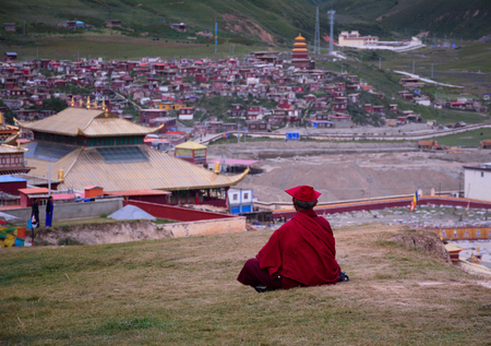 Tibetan monks sitting on the hill and looking at Yarchen Gar in Sichuan, China. Yarchen Gar is the...