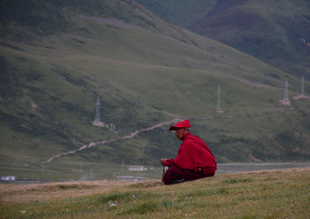Sichuan, China - Aug 18, 2016. A Tibetan monk sitting on the hill and looking at Yarchen Gar in Sichuan, China.のeditorial素材