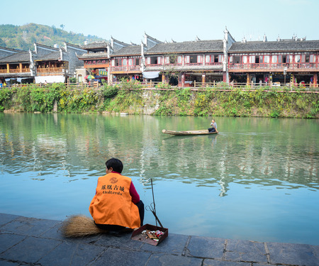 Hunan, China - Nov 6, 2015. A cleaning staff sitting on the riverbank at Fenghuang Old Town in Hunan, China.のeditorial素材