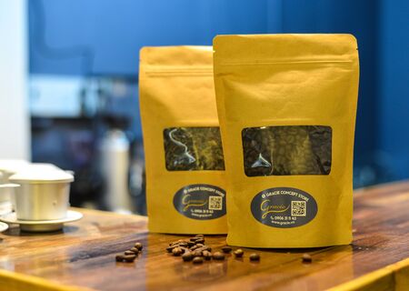Saigon, Vietnam - Sep 22, 2019. Brown kraft paper pouch bag with coffee beans in transparent window on wooden background.のeditorial素材