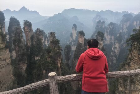 A man in red jacket seeing the rock mountains at Zhangjiajie National Park in Hunan China. Zhangjiajie is considered one of the most beautiful places in China.のeditorial素材