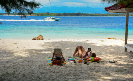 Gili, Indonesia - Apr 17, 2016. Young women reading on beach in Gili Islands, Indonesia. Gili is known for its beautiful white sand beaches, and colorful coral reefs.のeditorial素材