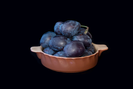 Plums in a round clay bowl on a black background. Studio lights, place for text.の写真素材
