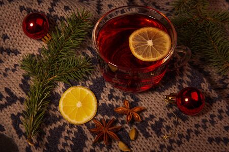 New year Christmas background. This is a glass Cup filled with a red drink with a slice of lemon, standing on a warm scarf, Christmas decorations, cardamom, star anise.の写真素材