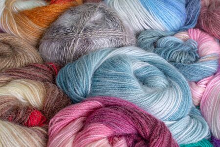 Close- up photo of many colorful rolls of knitting threads made of soft fluffy yarn. Skeins of...