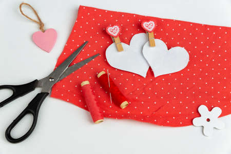 Two paper hearts, scissors, thread, a piece of cloth. Sewing supplies on a white background with an...
