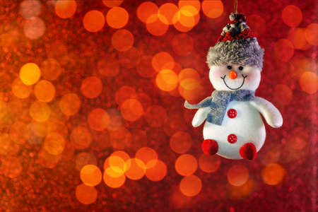 Funny white snowman on a red bokeh background. Bright red horizontal winter Christmas background. Winter holiday.の写真素材