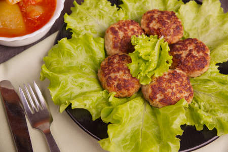 Cutlets and lettuce leaves on a black plate and cutlery. Home-made healthy food. Fried meatballs...