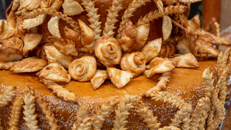 Food background. Toasted golden-yellow pie crust. A piece of white bread with a golden crust and flowers. The wedding, festive loaf is decorated with roses and ears.の写真素材