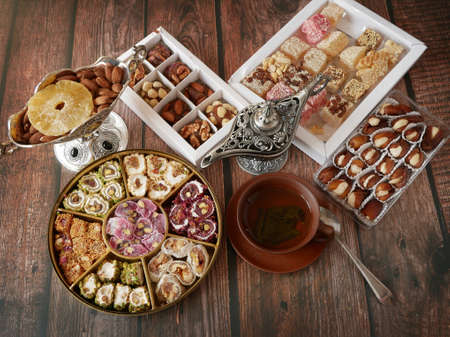 Eastern sweets in a wide range, Turkish delight with almond, traditional honey baklava, nuts, cashew and pistachio nuts on plates on wooden background. Pottery and silverware.の写真素材
