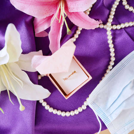 Wedding and coronavirus concept: jewelry box, blue medical mask, golden wedding rings and pink flowers bunchの写真素材