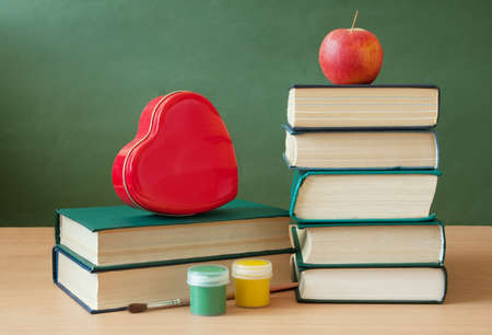 Book pile with apple, globe, pencils and sharpener on the school blackboard. Teacher's day concept