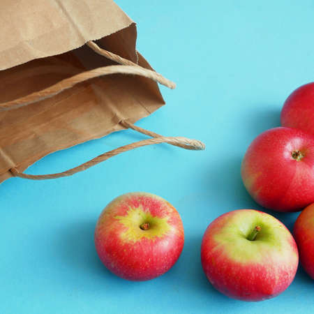 many red apples and paper bag on blue background, green grocery