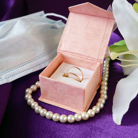 gift box, blue medical mask, golden wedding rings, pearls necklace and pink flowers bunch, Wedding and coronavirus concept, closeupの写真素材