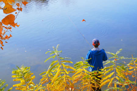 Autumn Fishing on a river. Young man relaxing and fishing, Amateur angler fishing on the autumn river, many alive fish in basketの写真素材
