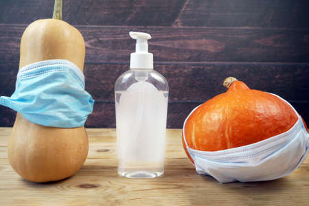 two pumpkins wearing a face mask for protection from coronavirus and sanitizer between. Social distance. Halloween 2020 concept, closeupの写真素材