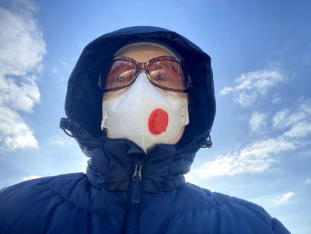 woman in high level protection respirator ffp3 and glasses on blue sky background, outdoors,...