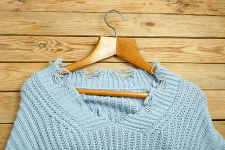 sweaters on hangers on wooden background with red price tag, winter sales concept, closeup