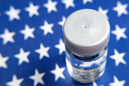bottle a vaccine is held by hand in a glove on background of the USA flag, vaccine against coronavirusの写真素材