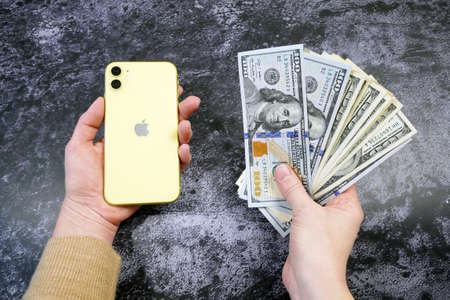 one hand takes stack of money and other hand takes mobile phone, closeupの写真素材