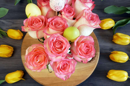 yellow tulips, roses and eatser eggs on wooden background, closeup