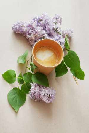 creative composition with morning coffee in paper glass and lilac flowers with green leaves around...