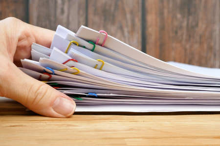 Hand takes stack of documents with binder clips wooden table