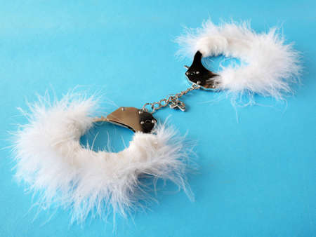 white fluffy handcuffs on blue background, gentle sexsual games concept, closeupの写真素材