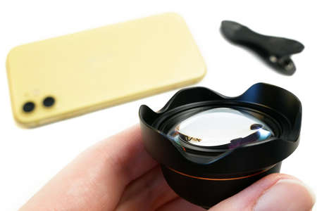 yellow smartphone with external lens on clip on white. An additional portrait lens and clip are supplied with the mobile phone, closeupの写真素材