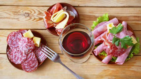 Red wine in glass and cold smoked meat plate, antipasto set platter wooden plate. Wine and cold...