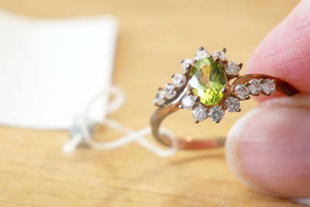 ring with peridot stone and diamonds in hands on wooden background, closeup