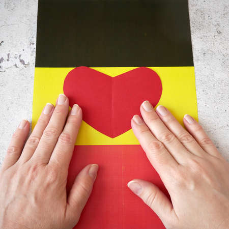 I love Germany. Hands puts red paper heart on Germany flag background. Day of German Unity - 3 october, closeupの写真素材