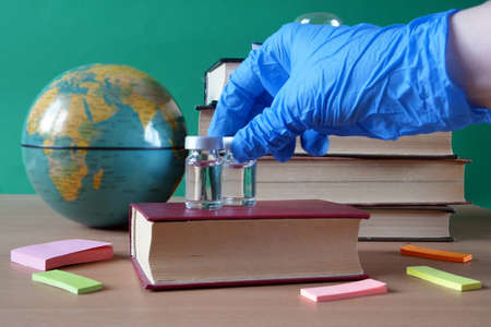 doctor puts in table bottles and syringes of vaccine aganist covid-19 near book pile and school...