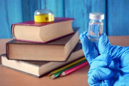 bottles and syringes of vaccine aganist near book pile and school supplies, back to school in time concept, closeupの写真素材