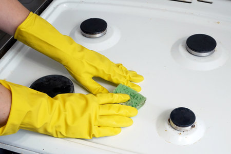 Woman hands in yellow gloves washing gas stove in the kitchen with a sponge, washing and cleaning...