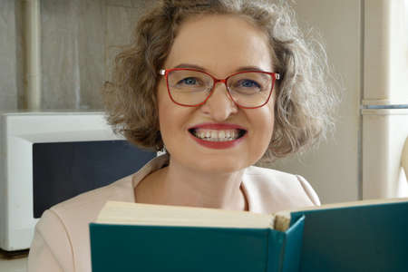 middle aged woman in glasses make the lesson with books at her home at kitchen, lesson for pupils and students online, closeup, conceptの写真素材