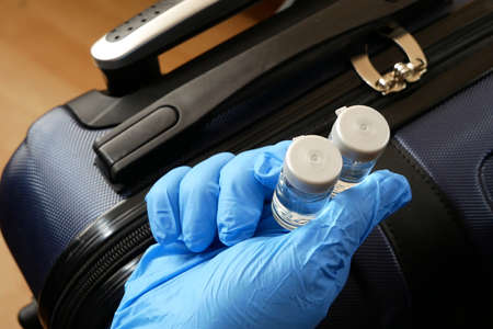 hand in medical gloves takes two bottles on vaccine on suitcase background, vax in airoport concept,...