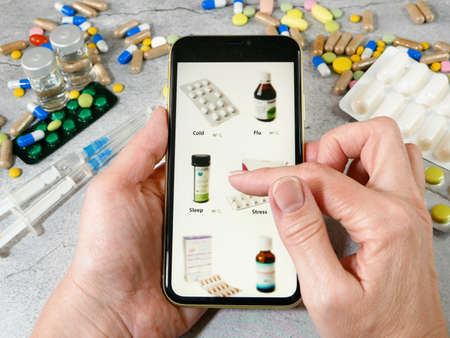 hand takes phone and search medications on pills and drugs background, online pharmacy concept, closeupの写真素材