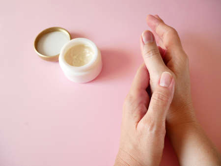woman applying cream on her hands on pink background, cold season hands skin protection. Hand skin care concept. Natural organic beauty products. Top view closeupの写真素材