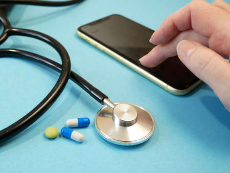 Pills and stethoscope on smartphone on blue background, concept of telemedicine or e-health, closeup