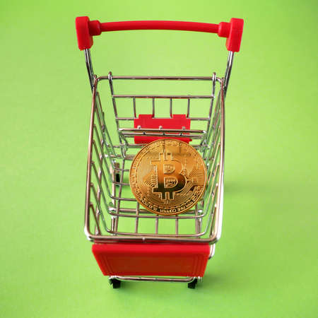 Shopping trolley for purchases with bitcoins. Crypto currency bitcoin in the baby chair in trolley on a green background, top viewの写真素材