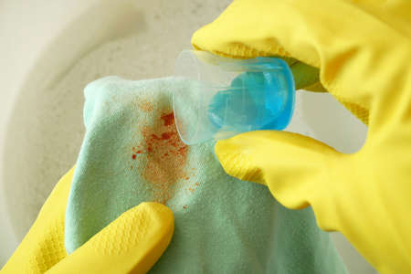 Cleaning laundry manually. Women's hands in gloves washing dirty stained on colored cloth with a stain remover and soak in soapy water, closeupの写真素材