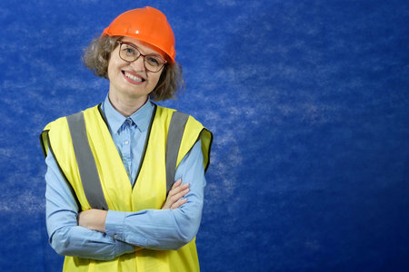 Feamle Engineer in the construction helmet and yellow vest with mobile phone and documents on blue background, closeupの写真素材