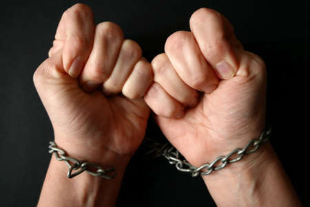 hands clenched into fists in handcuffs in the form of chains on a black background, the problem of...