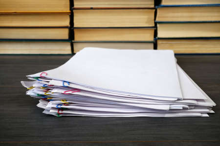 stack of documents with binder clips and books pile wooden table, closeup